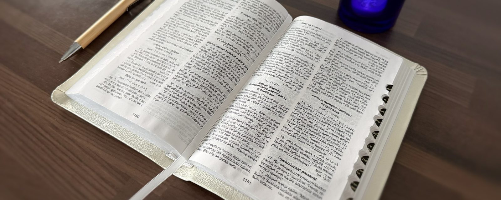 En uppslagen bibel på ett bord, bredvid en penna och ett brinnande ljus.